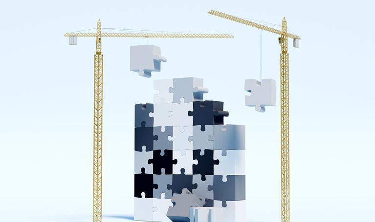 Construction cranes are actively lifting and placing puzzle pieces, slowly constructing a towering, upright puzzle.