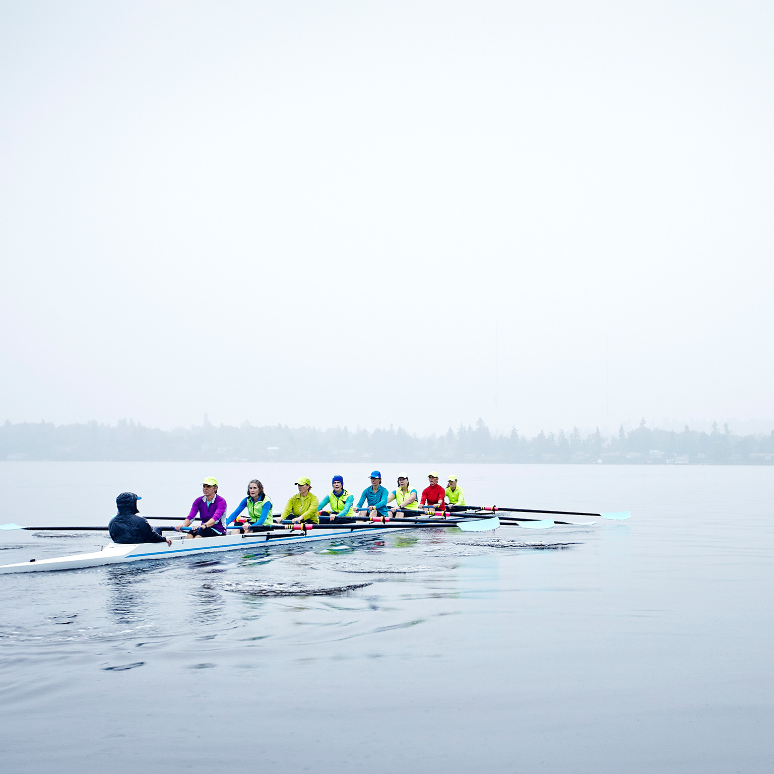 Group of mature female rowers rowing eight person boat during rainy morning practice