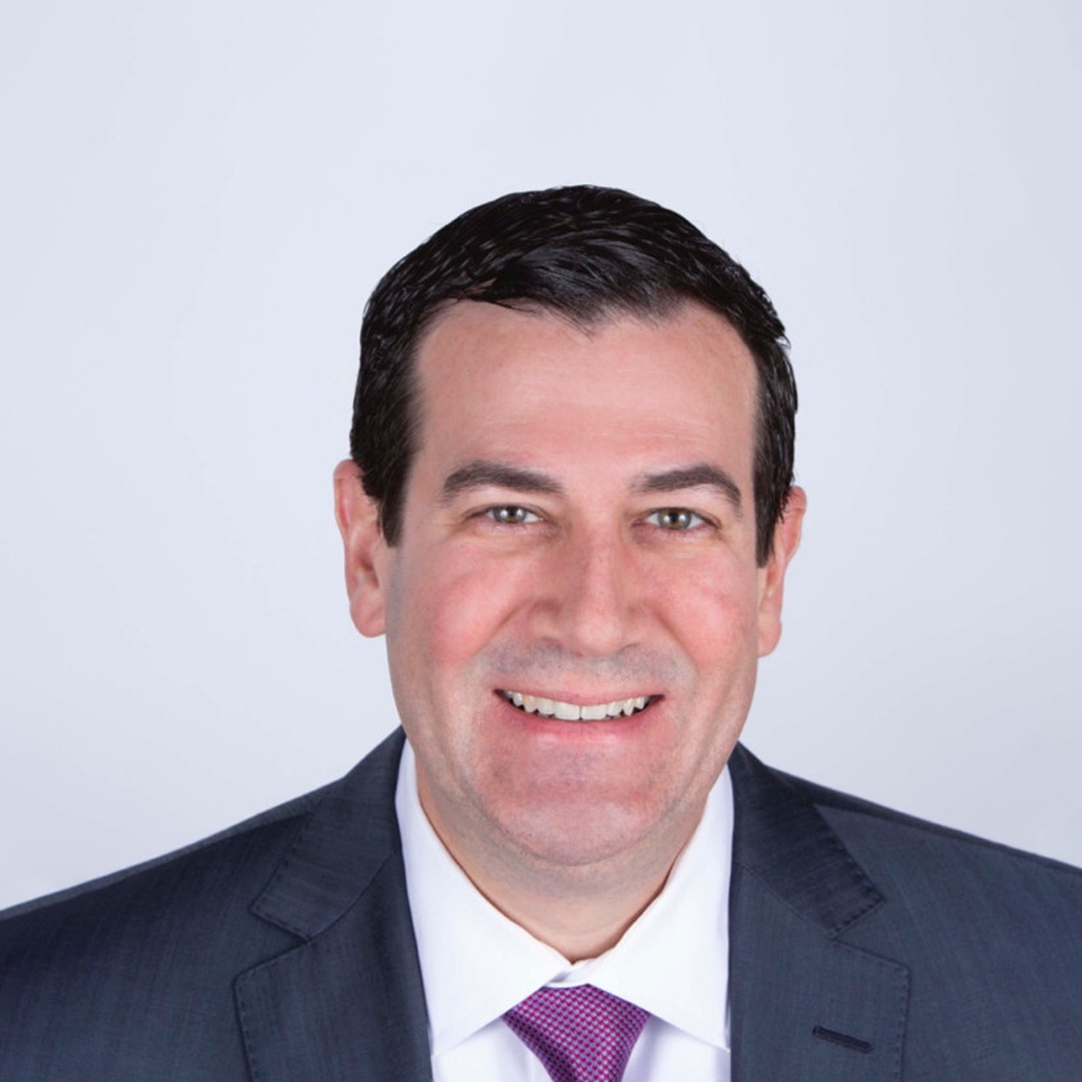 Portrait of Mark Birkhead with a light smile, wearing a charcoal suit and a maroon tie.