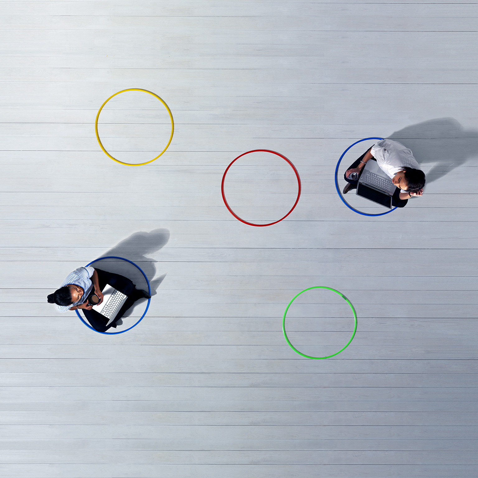 Business women with laptops sitting across the room from each other in 2 of 5 multi-colored circles