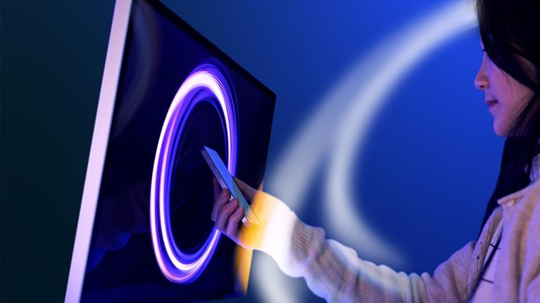 Woman interacting with circular patterned light swirling around and a screen with a similar light pattern displayed.