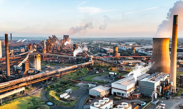 Steel mill emitting smoke and steam at sunset