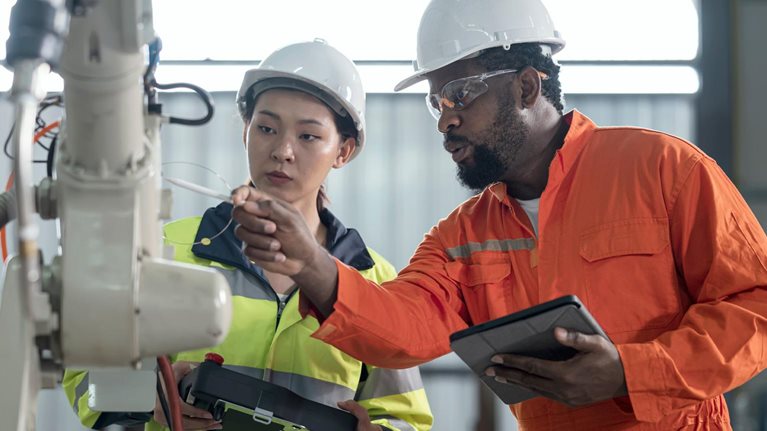 man and woman inspecting safety of robotic arm in factory