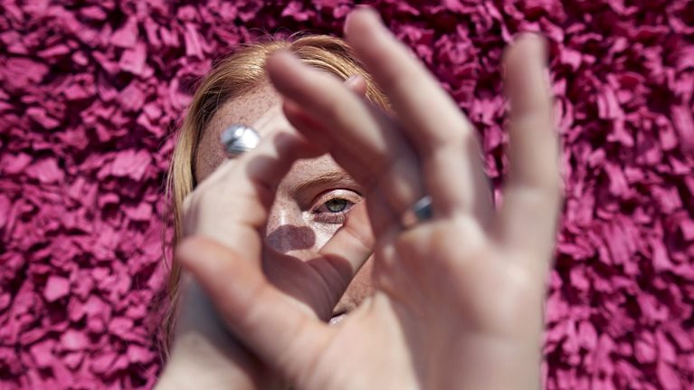 Image of a woman looking through her hands like a telescope with a textured wall behind her.