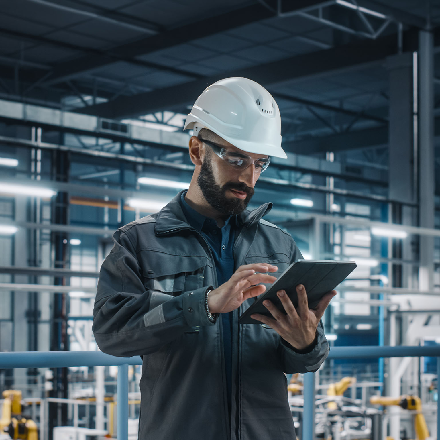 Portrait of Automotive Industry Engineer in Safety Glasses and Uniform Using Laptop at Car Factory Facility. Professional Assembly Plant Specialist Working on Manufacturing Modern Electric Vehicles.