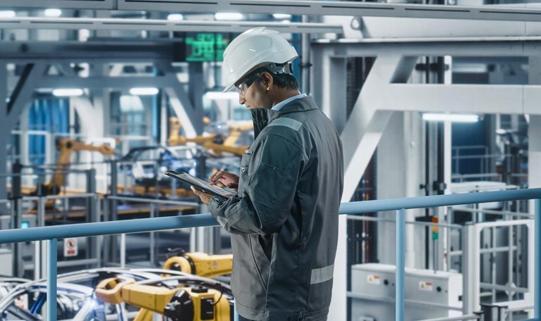 Car Factory Engineer in Work Uniform Using Tablet Computer. Automotive Industrial Manufacturing Facility Working on Vehicle Production with Robotic Arms. Automated Assembly Plant.