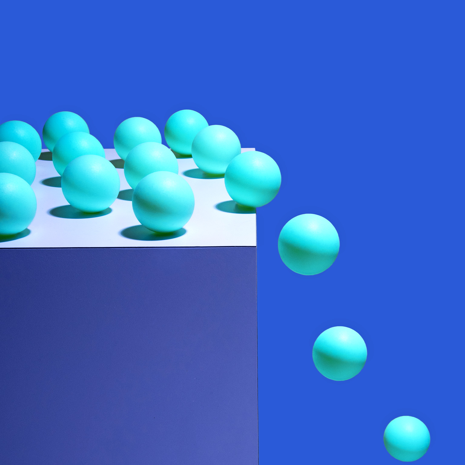 Multiple balls on top of a box with a few of them rolling and falling off the edge.