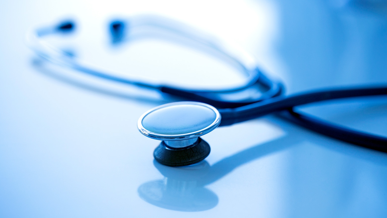 Tight focus shot of a stethoscope on a reflective desk.