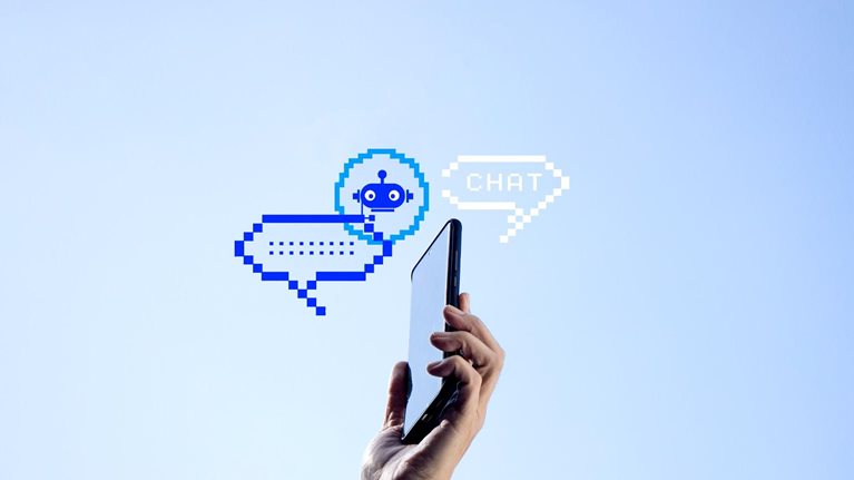 A hand holding a mobile phone with two pixelated chat bubbles and an AI bot icon against a clear blue sky.