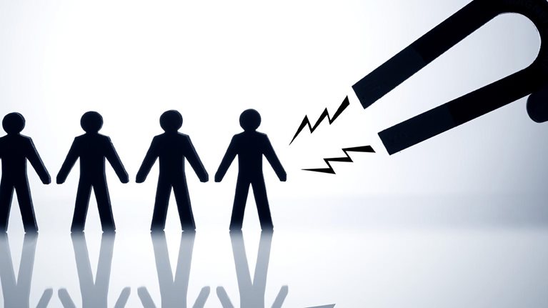 A hand holding a horseshoe magnet trying to attract a row of figures in the shape of people.