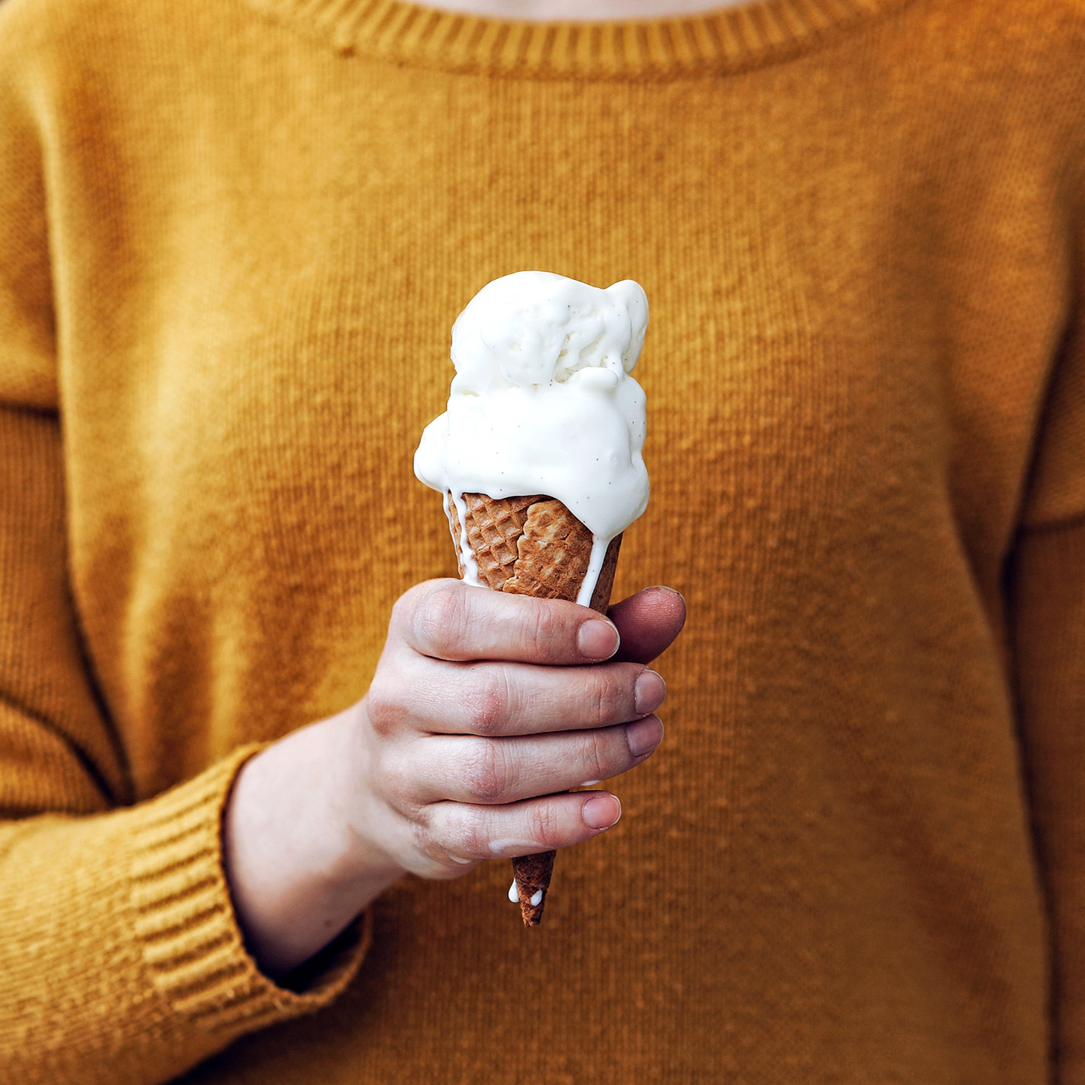 Woman in yellow sweater holding a melting ice cream cone in her hand