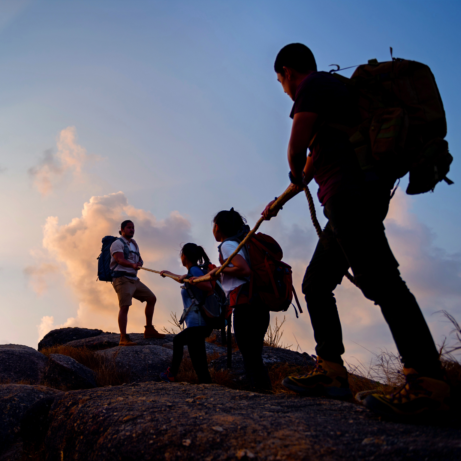 Group of friends hikers climbing up silhouette mountain cliff.