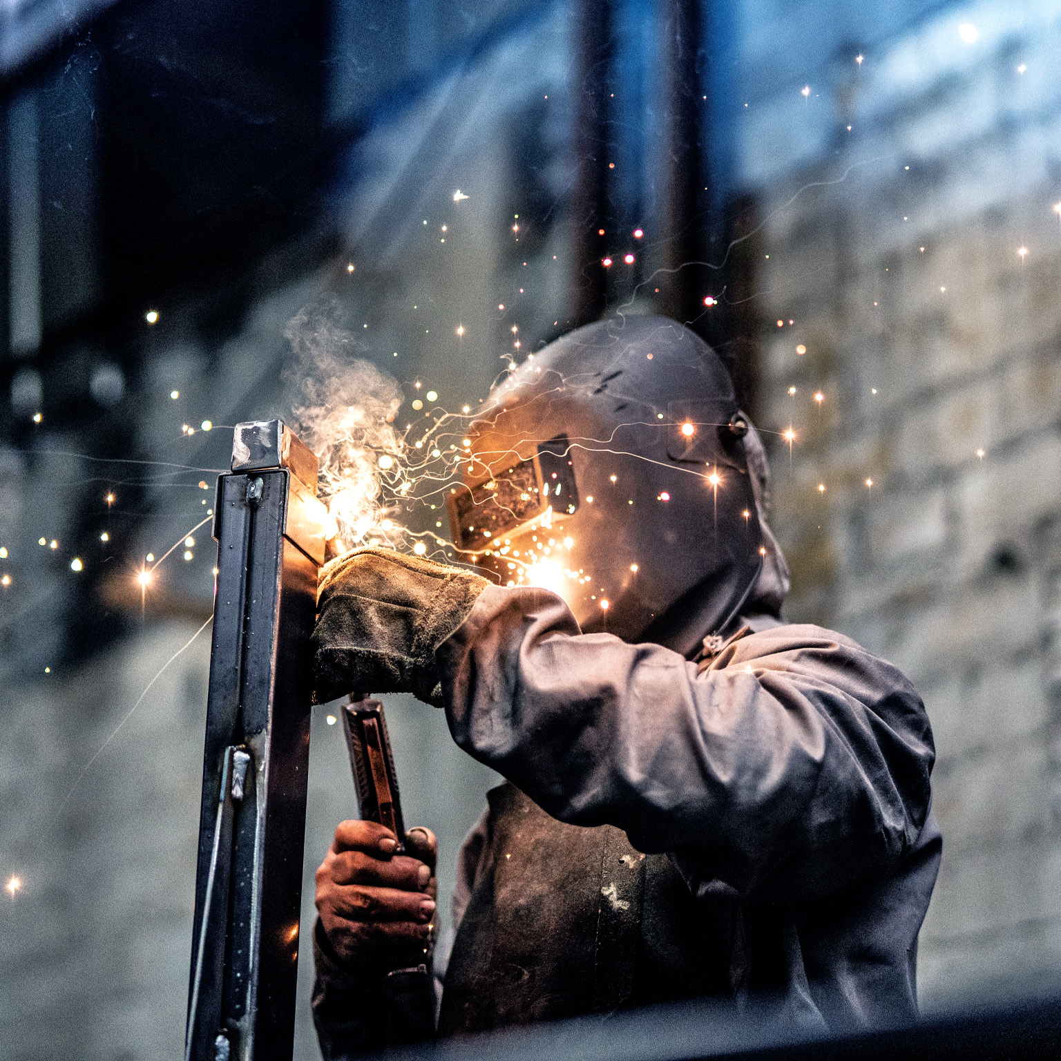 An individual clad in protective welding attire, working on a steel component while sparks scatter.