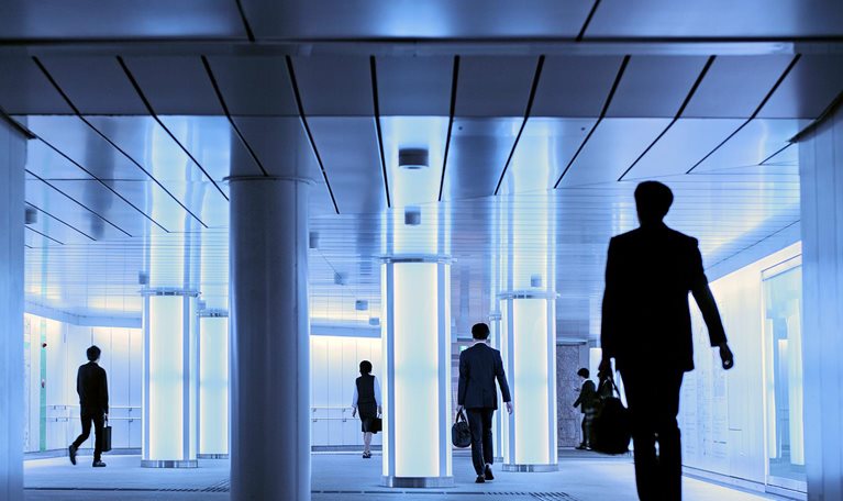 Silhouettes of people walking in a well lit hallway