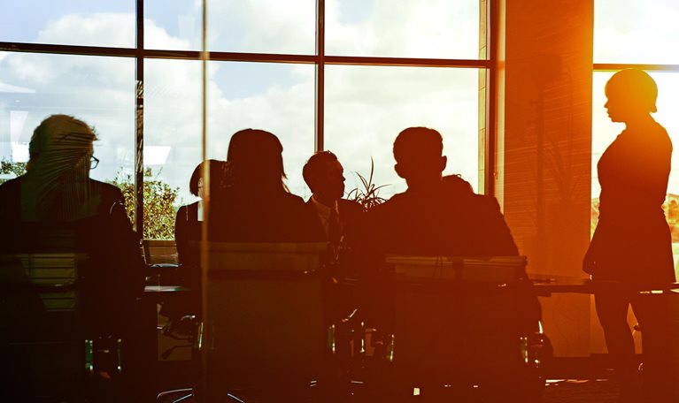 The sun is setting on workers in glass-walled boardroom
