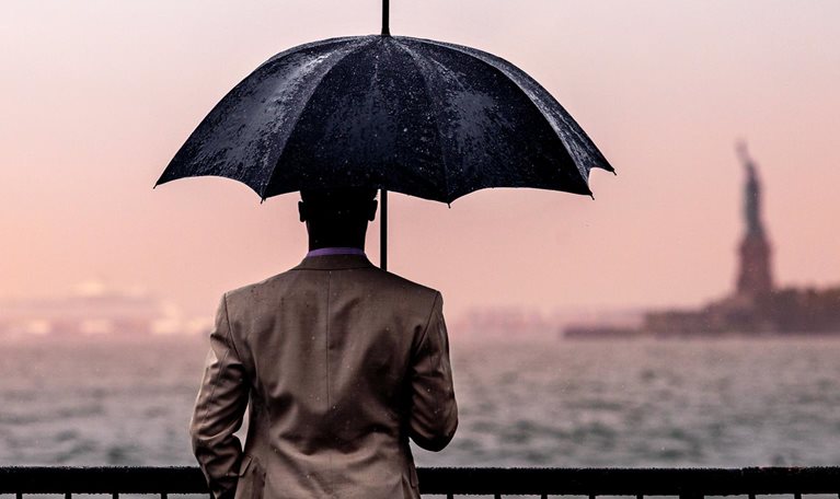 Rear view of man with umbrella standing by railing against sea.