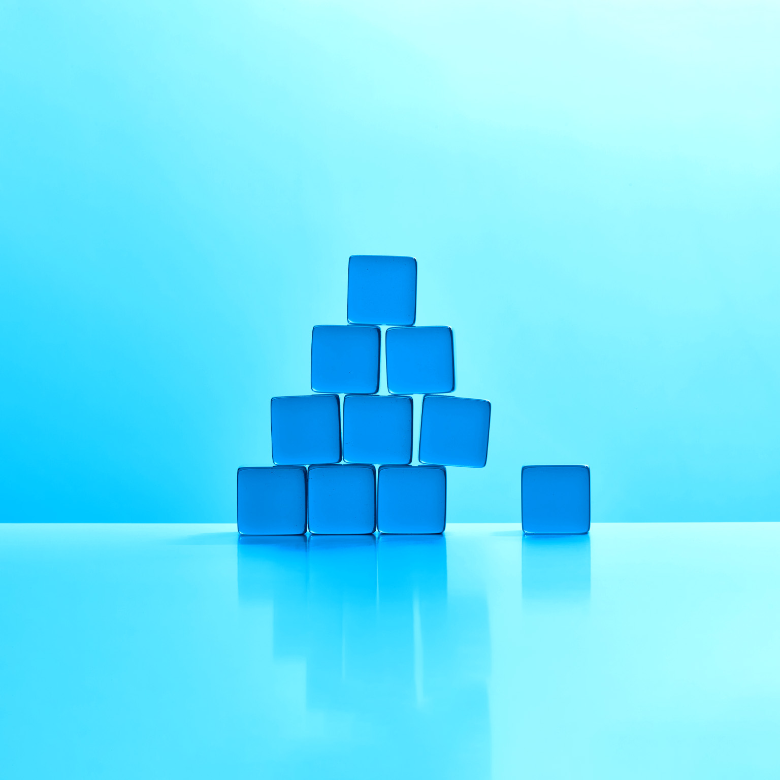 A triangular stack of blue acrylic cubes. The bottom right cube has been removed and causing the stack to become unstable.