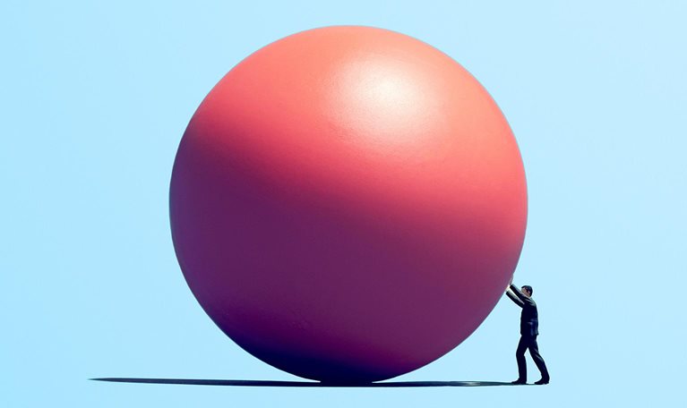 Person pushing a large pink sphere across a flat surface against a light blue background.