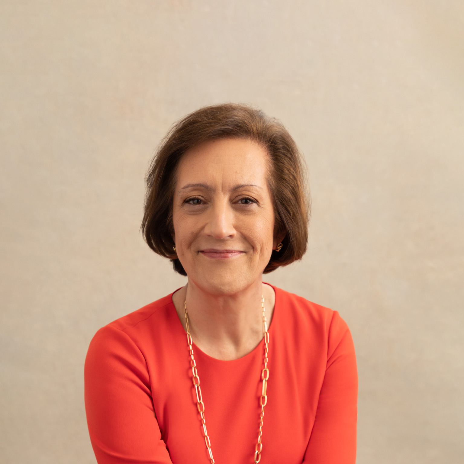 A smiling Judy Marks in a sophisticated red fitted top and a gold link chain around her neck.