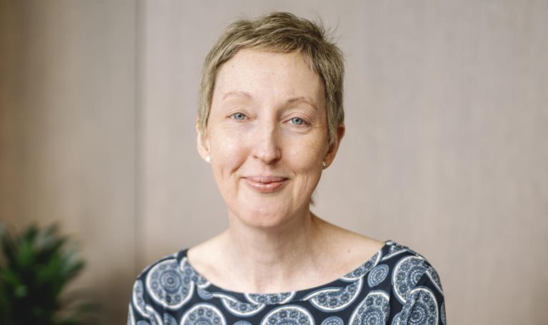 The camera captures CEO Anna Manz's serene smile, framed by her short blonde hair and bright blue eyes. She is wearing a dark blue top with a circular pattern.