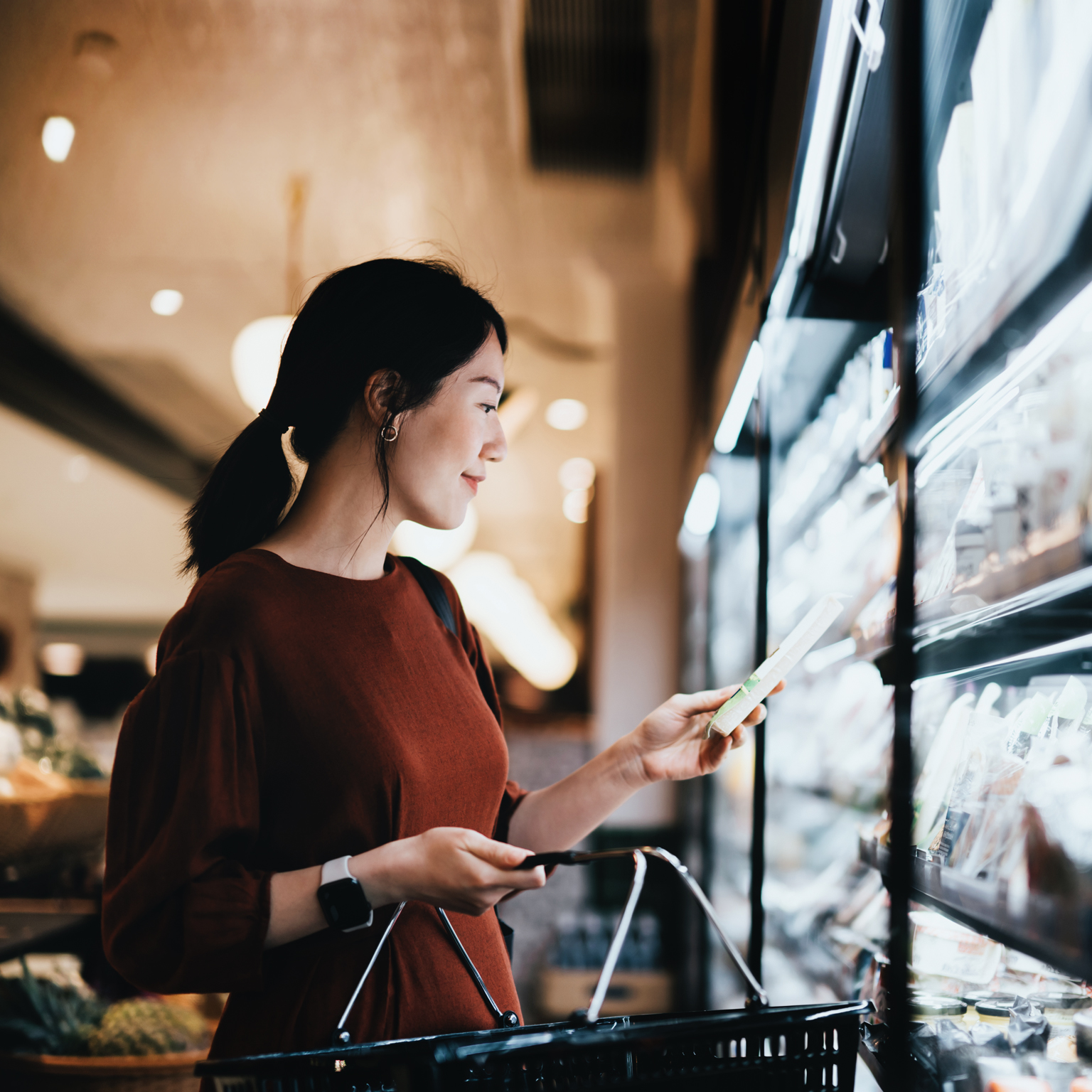 Young Asian woman carrying a shopping basket while grocery shopping in supermarket