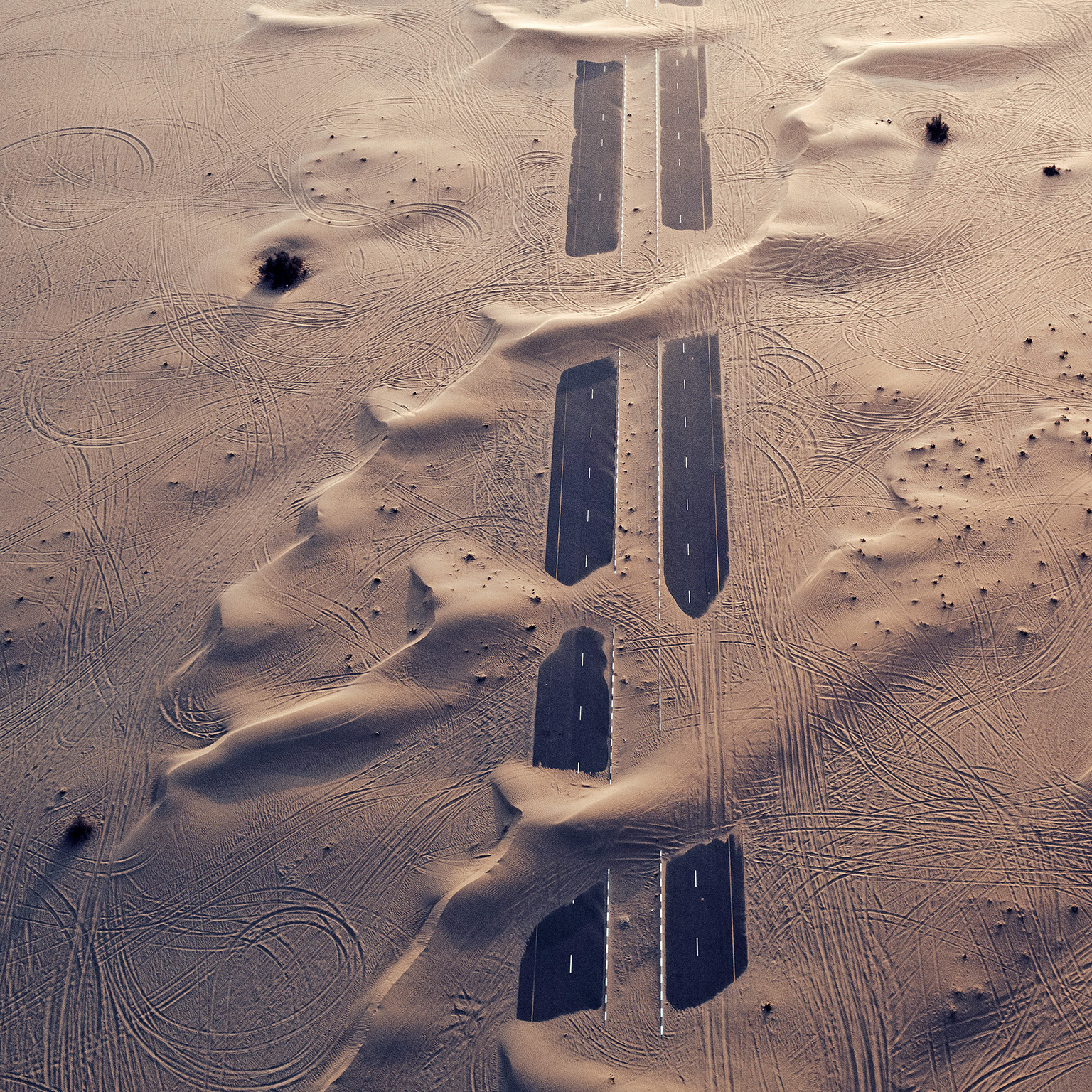 Sandy terrain with a road emerging in parts between stretches of sand.