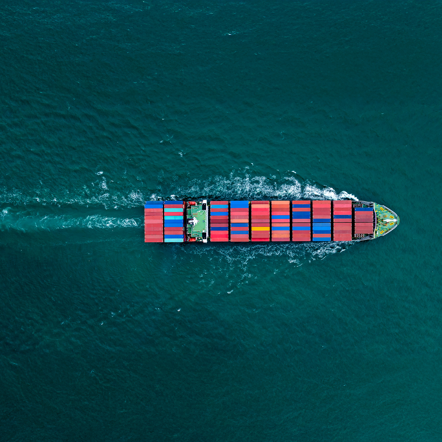 Overhead view of a large container ship sailing with many stacks of colorful containers visible on board