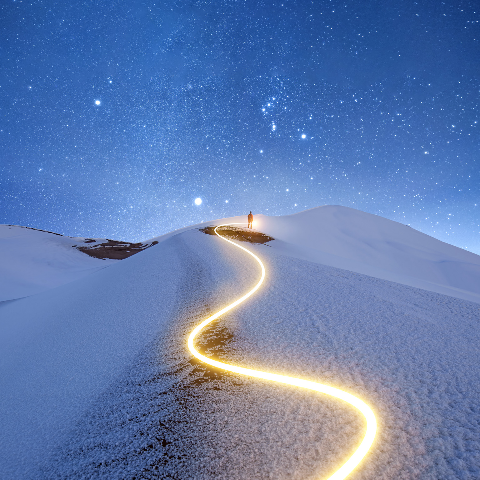 A solitary figure stands upon a snow-covered peak against a starry night sky. A zig-zagging light trail marks the path taken by the figure to reach the summit.