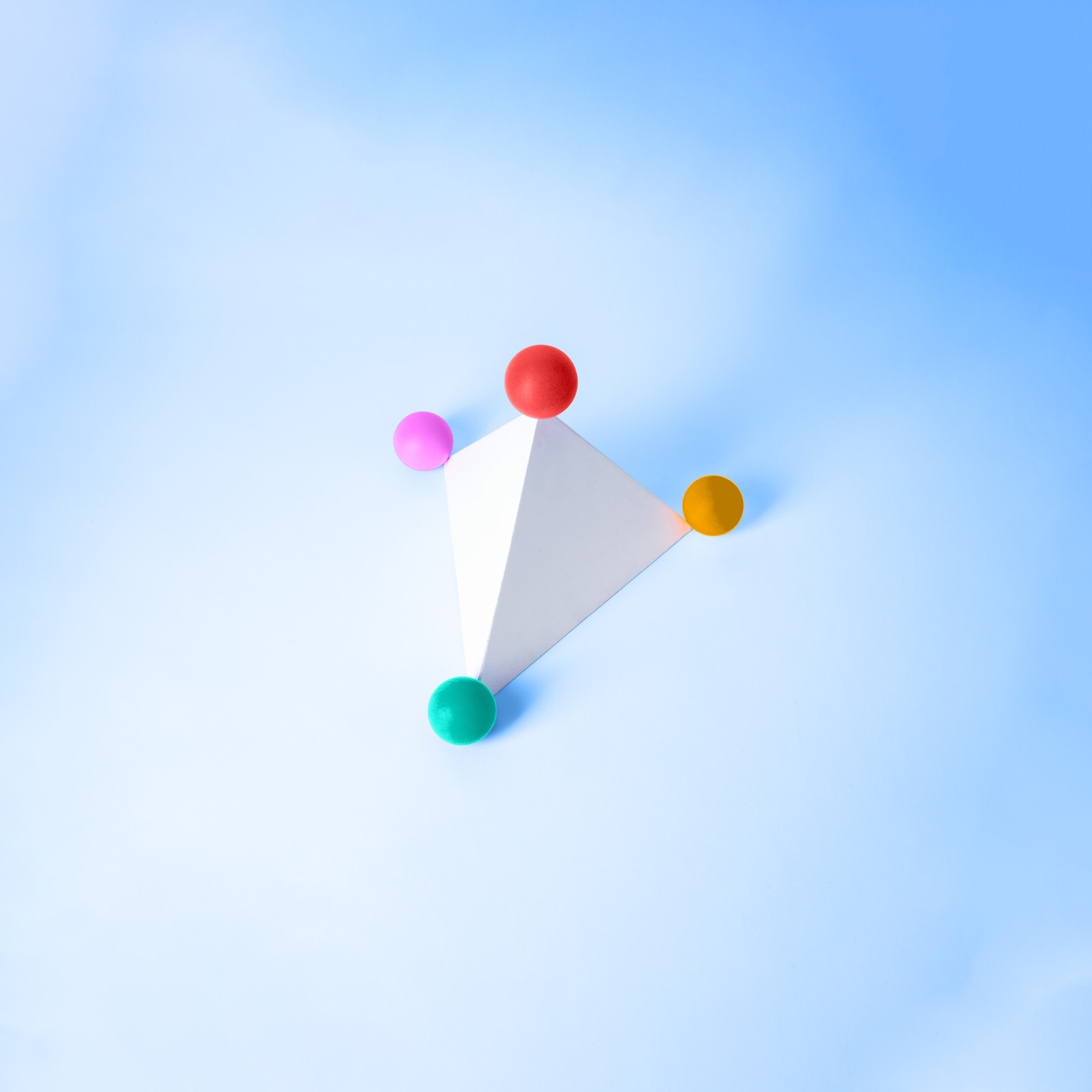 A white triangular pyramid with four balls of varying colors situated at each of the pyramid's points. 