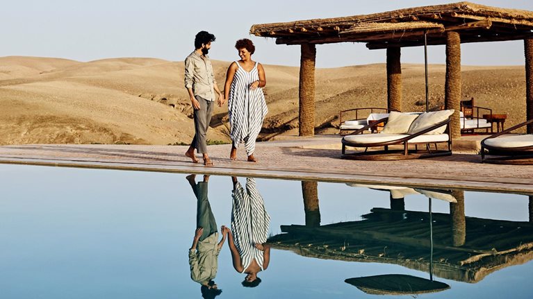 A couple walking around pool at desert camp at sunrise