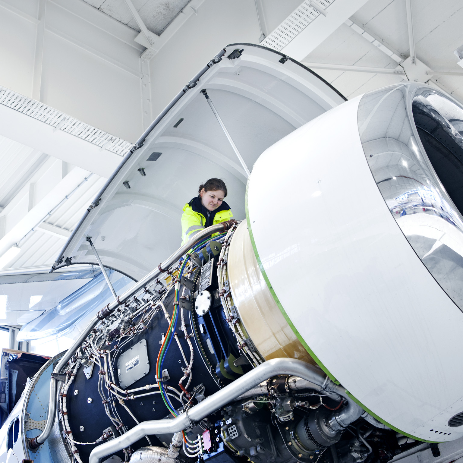  An engineer working on the engine of a commercial airliner in a large, airy hanger. 