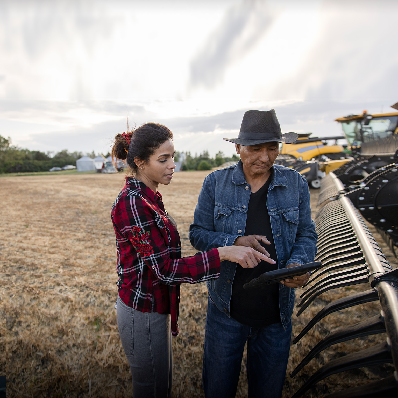 Farmer couple with digital tablet at combine harvester on farm - stock photo