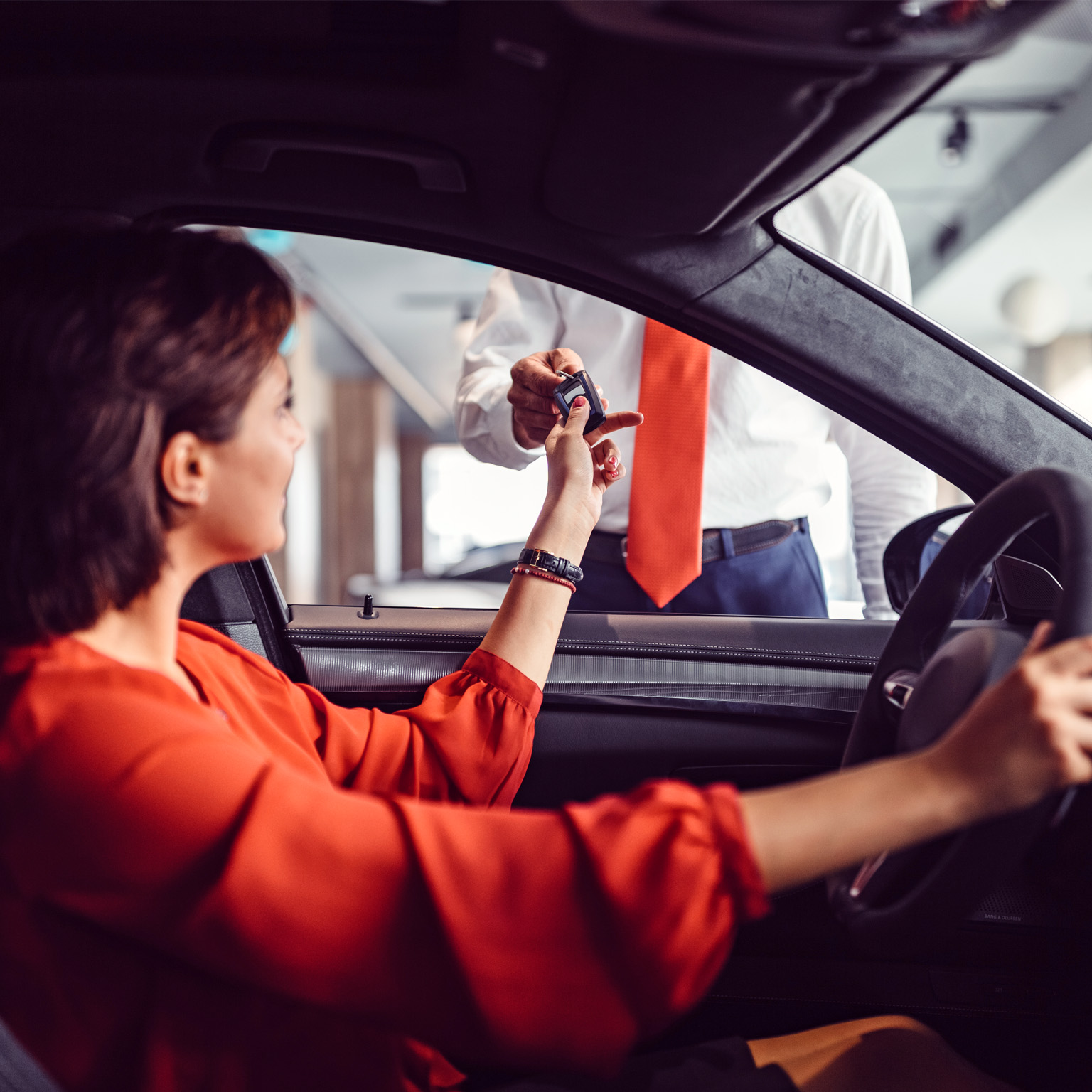 Woman in car handing car keys to a man standing outside