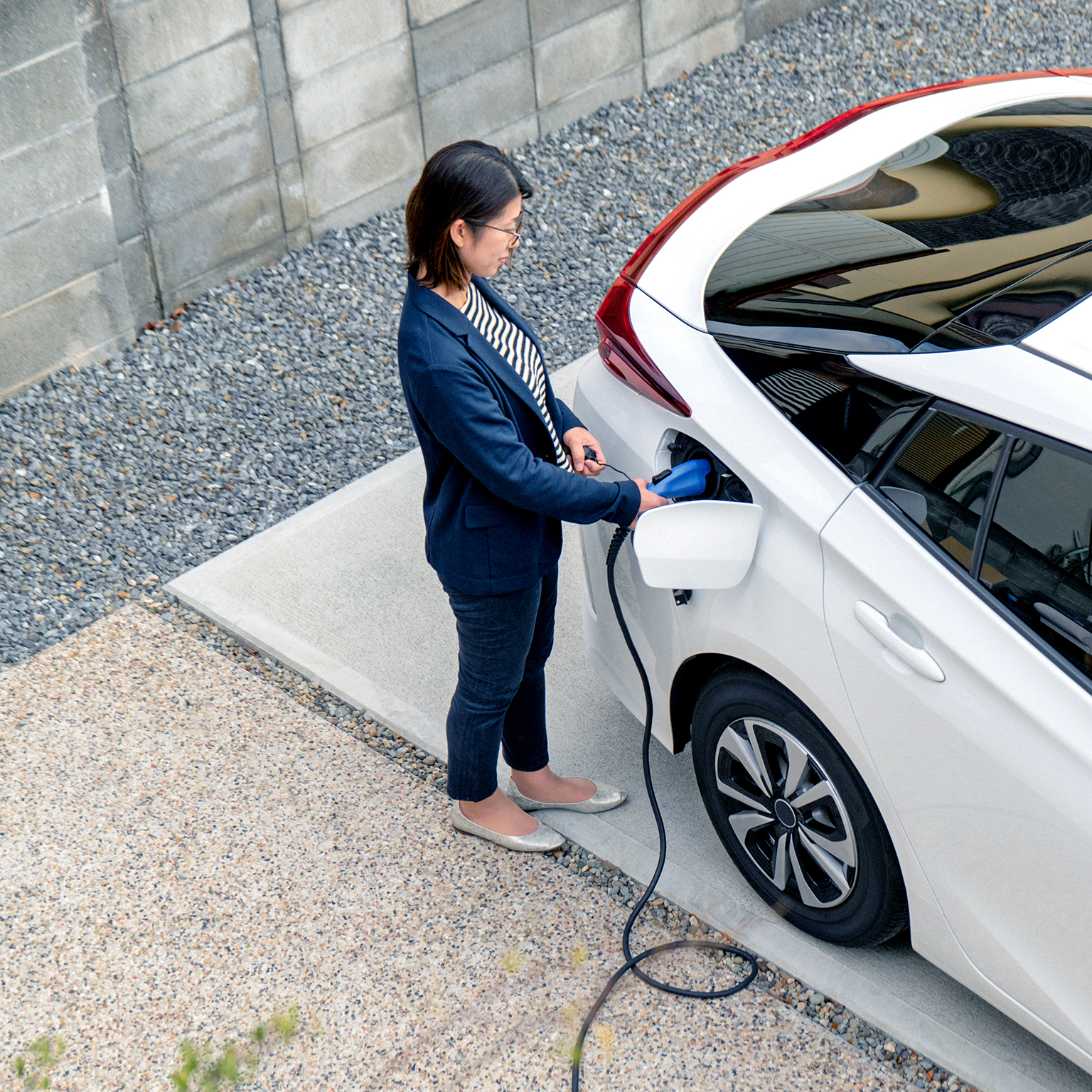 Mid adult woman charging her electric car at home - stock photo