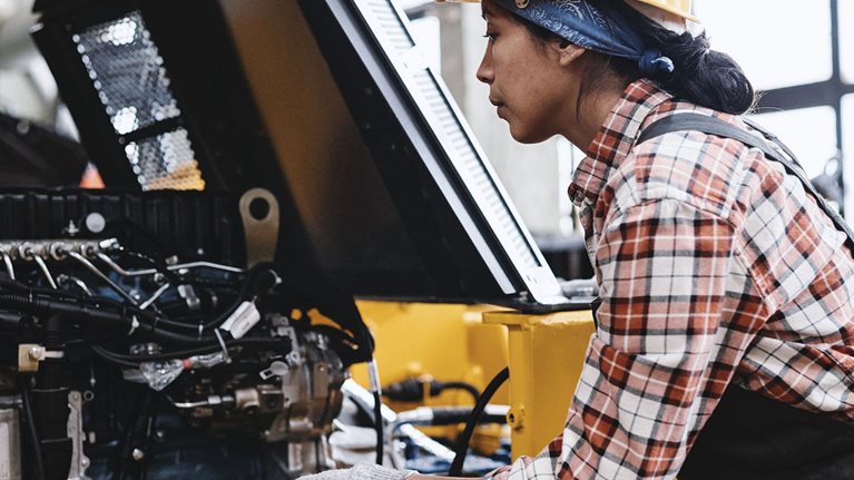 Young female technician in coveralls and hardhat checking motor of machine