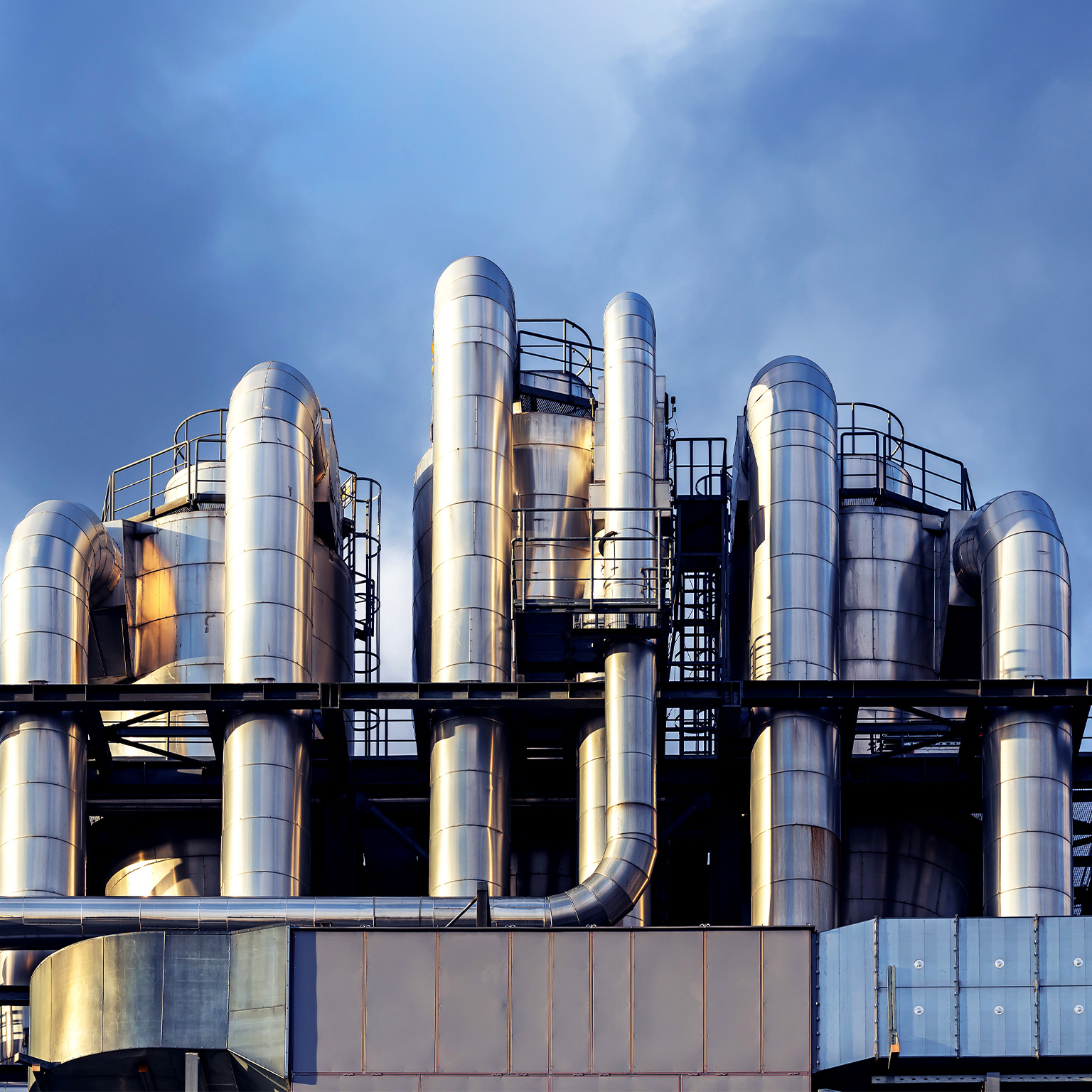 Image of interwoven chemical pipes at a factory shining in the sunset.