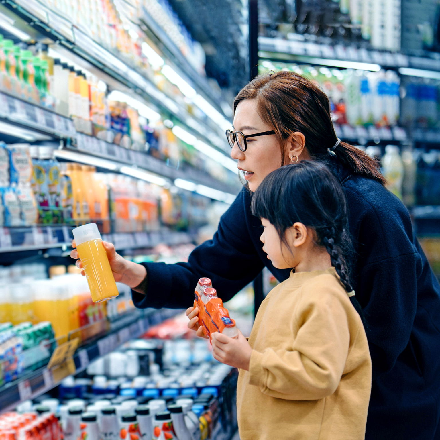 A lady and a young girl checking bottled drinks, including probiotics, from the shelves of a departmental store.