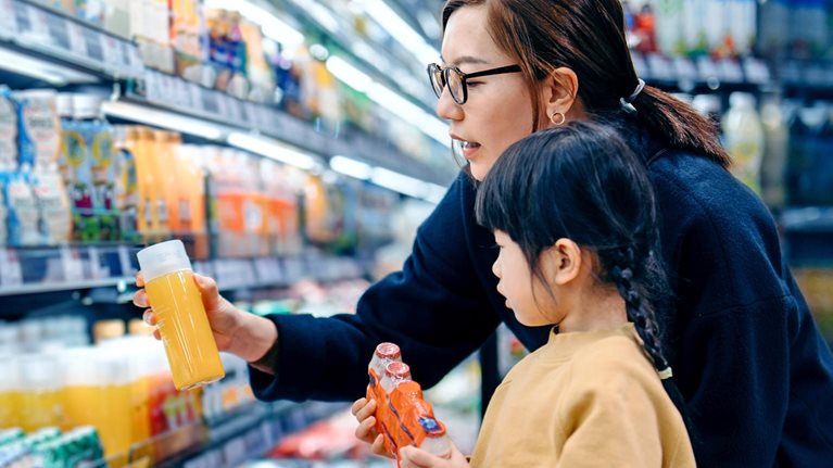 A lady and a young girl checking bottled drinks, including probiotics, from the shelves of a departmental store.