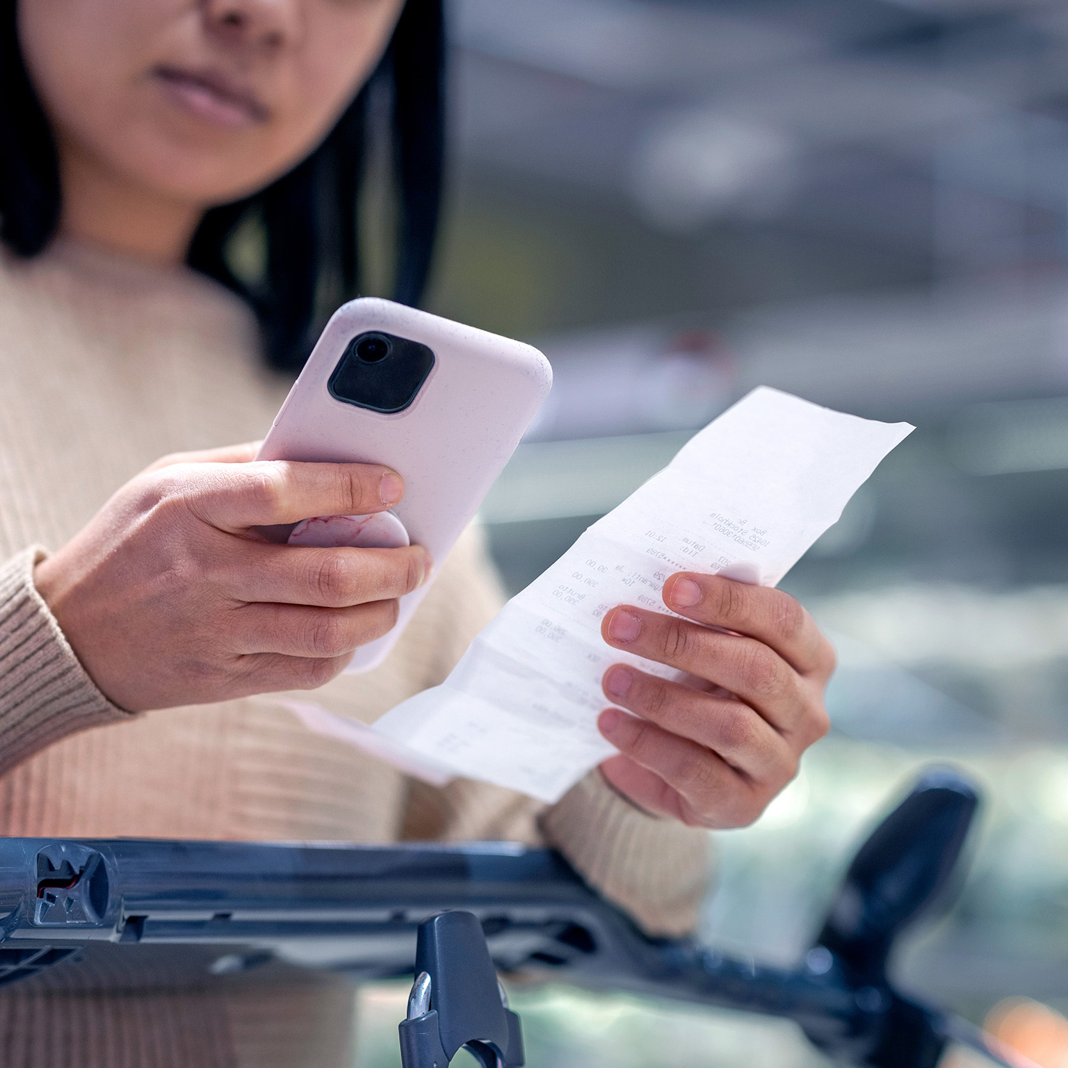 Young woman examining list while using smart phone at supermarket