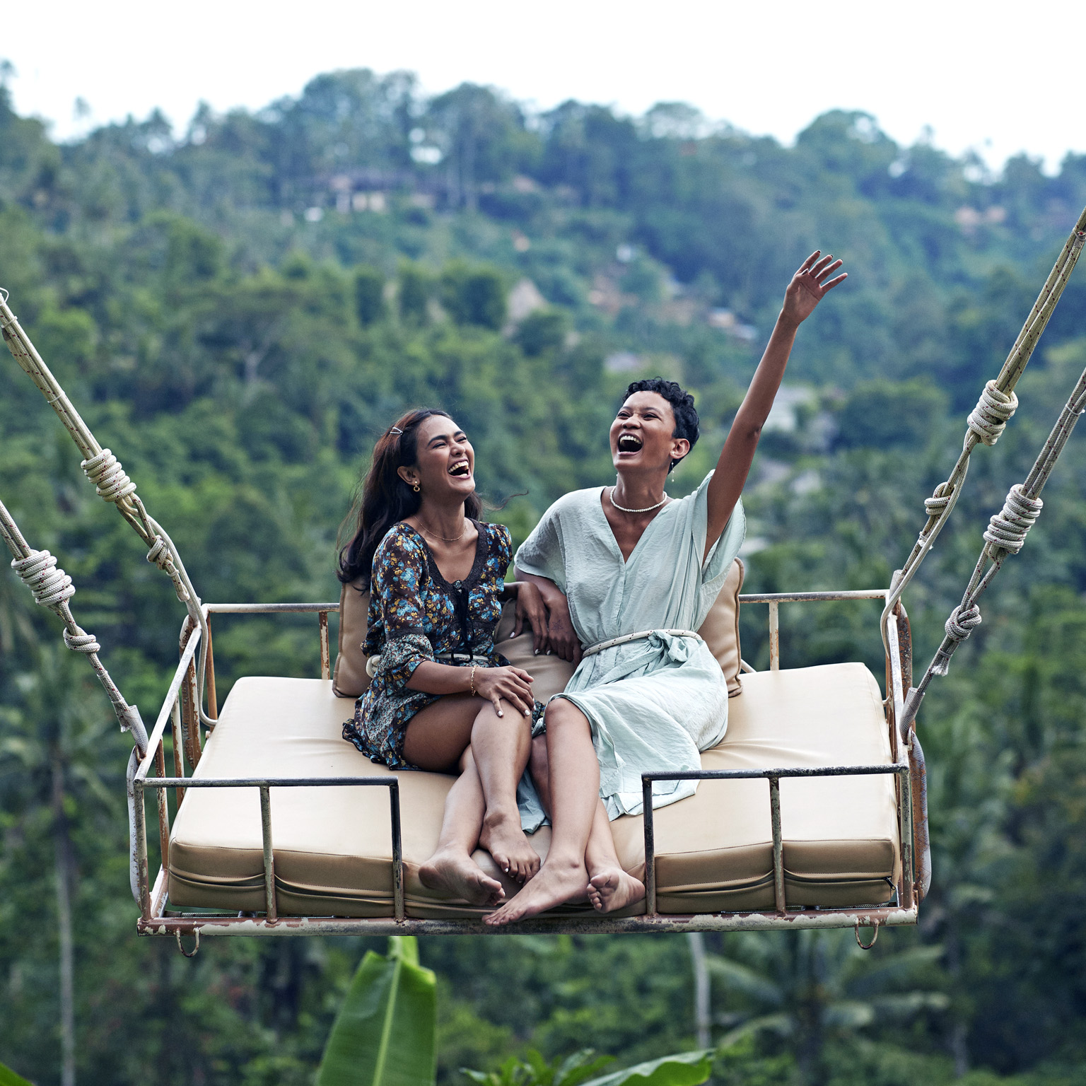 Two women sit on a swing enjoying jungle views while on vacation