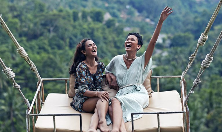 Two women sit on a swing enjoying jungle views while on vacation