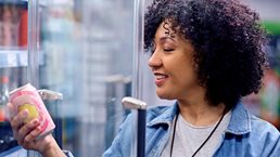 Happy woman holding a can of soda at refrigerated section in a supermarket