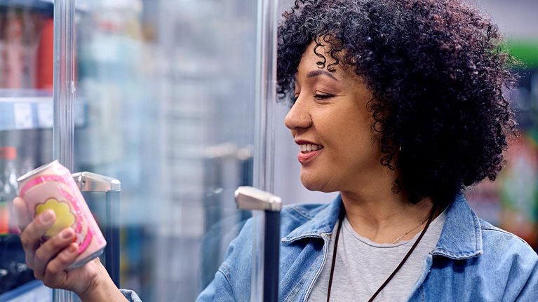 Happy woman holding a can of soda at refrigerated section in a supermarket