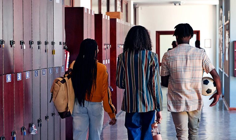 Full length rear facing view of male and female students walking together in school hallway with lockers