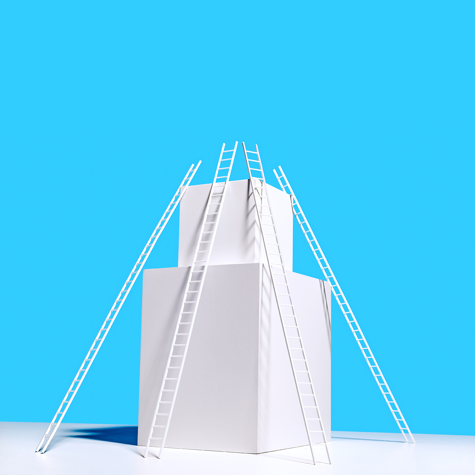 4 long white ladders resting on 2 stacked white boxes on white surface, blue background