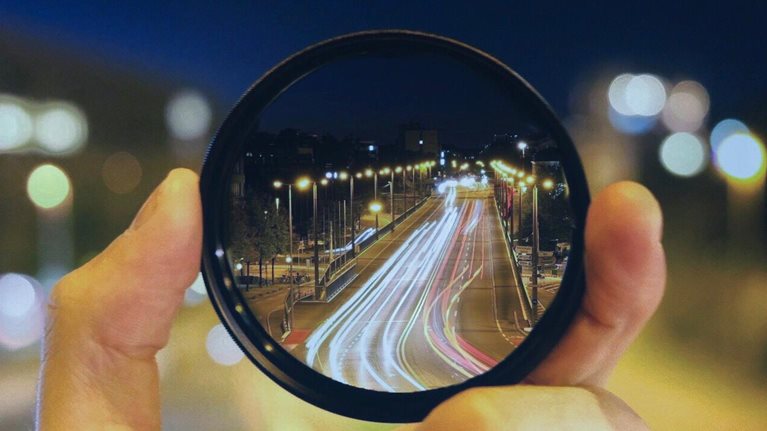 Close-Up Of Hand Holding Lens Against Road At Night