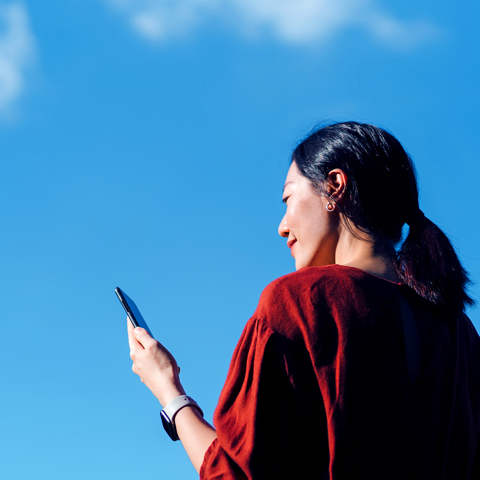 Low angle portrait of young Asian woman using smartphone against beautiful blue sky