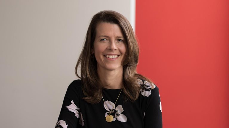 Portrait of a smiling Barbara Karuth-Zelle resting her elbow on a wooden table.