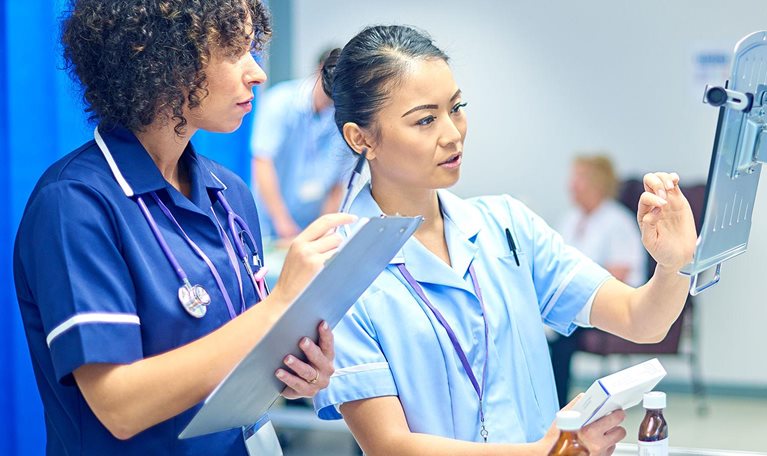 A young nurse checks the dosage on her digital tablet supervised by her staff nurse