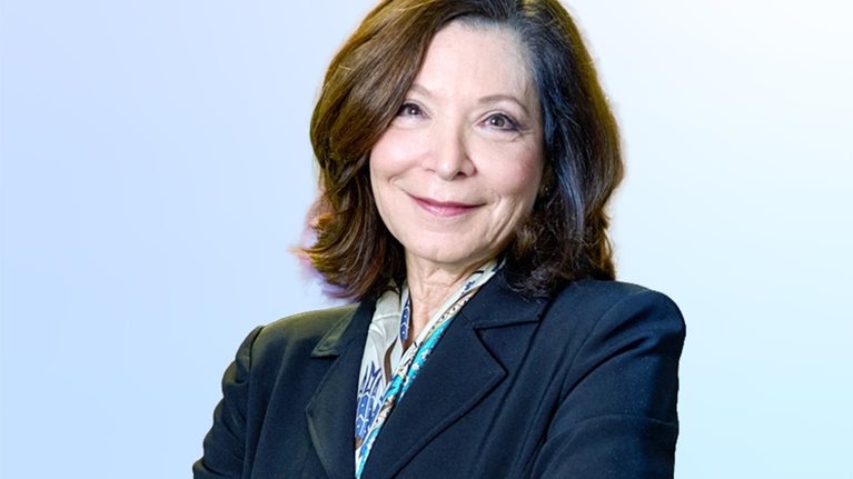 Leslie Davis wearing a blue jacket, arms folded, warmly smiling.